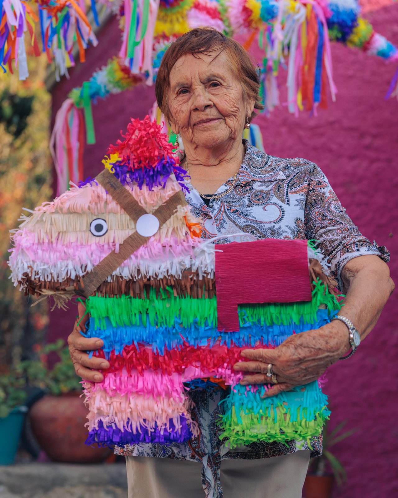 An older woman holding a classic donkey piñata in a pink courtyard, Mexico