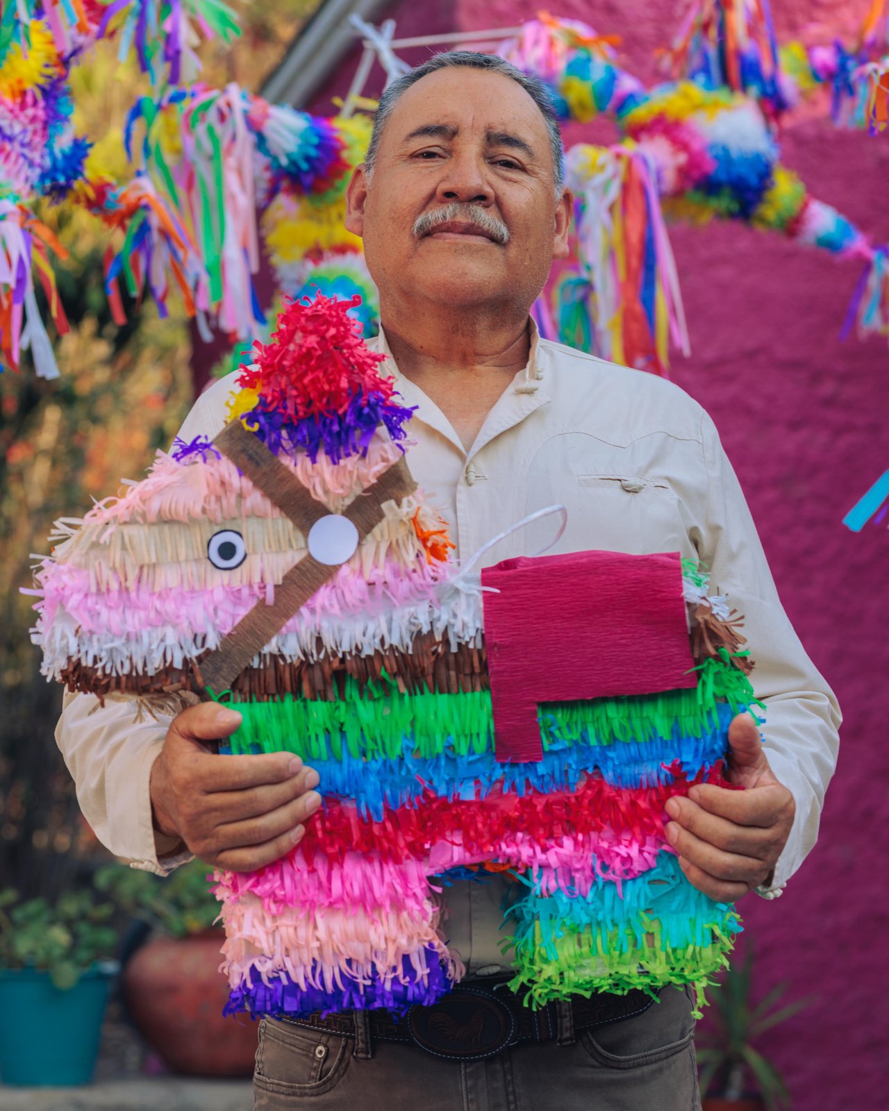 A man holding a colourful donkey piñata among his handiwork, Mexico