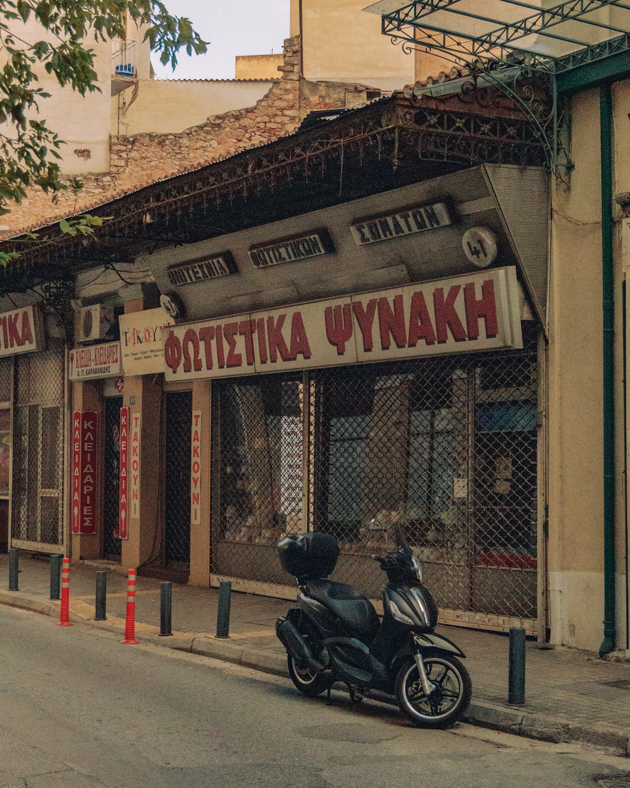 A shuttered Greek lighting shop with a parked scooter on a quiet street, Greece