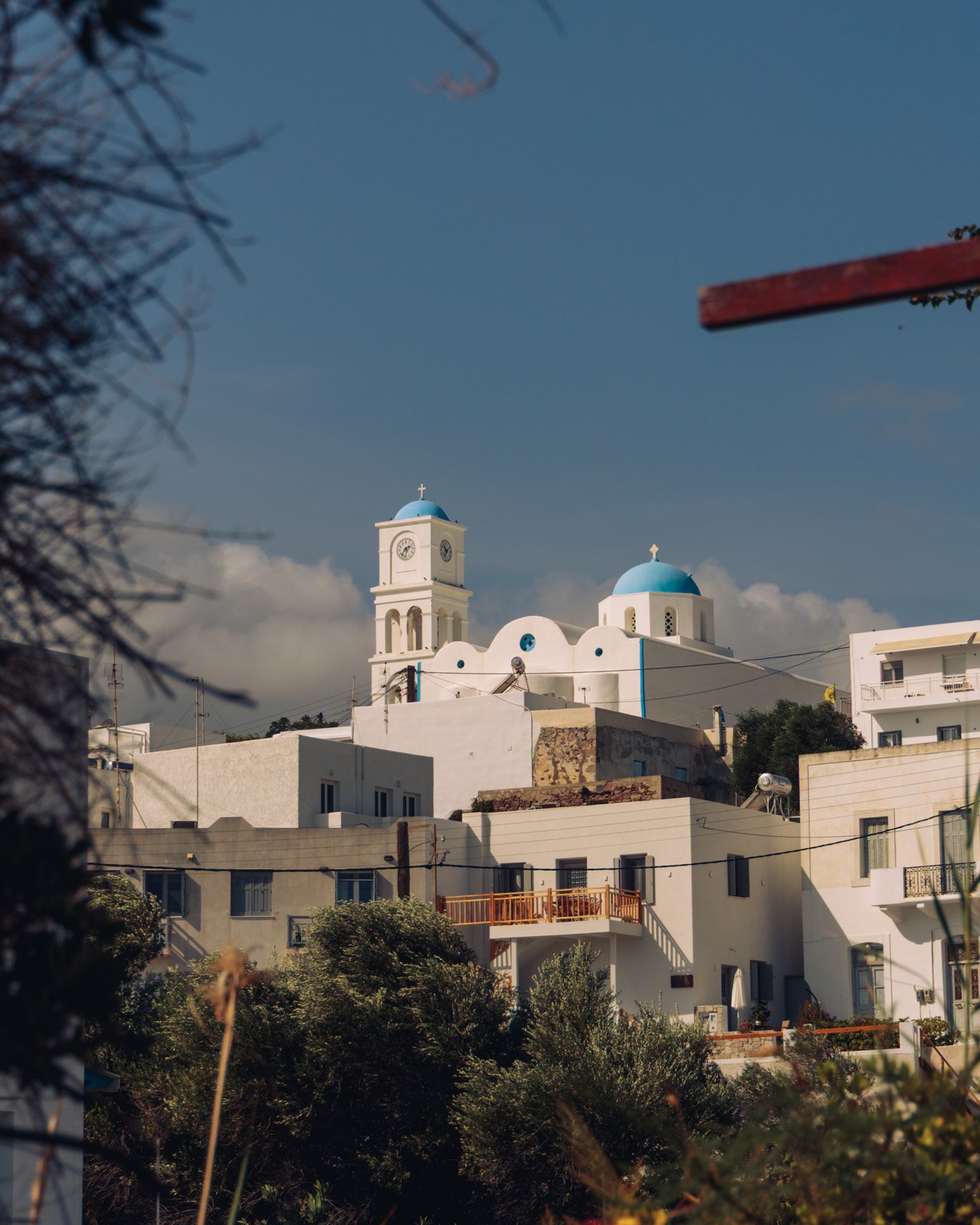 A hillside village of white houses with a blue-domed church and clock tower, Greece