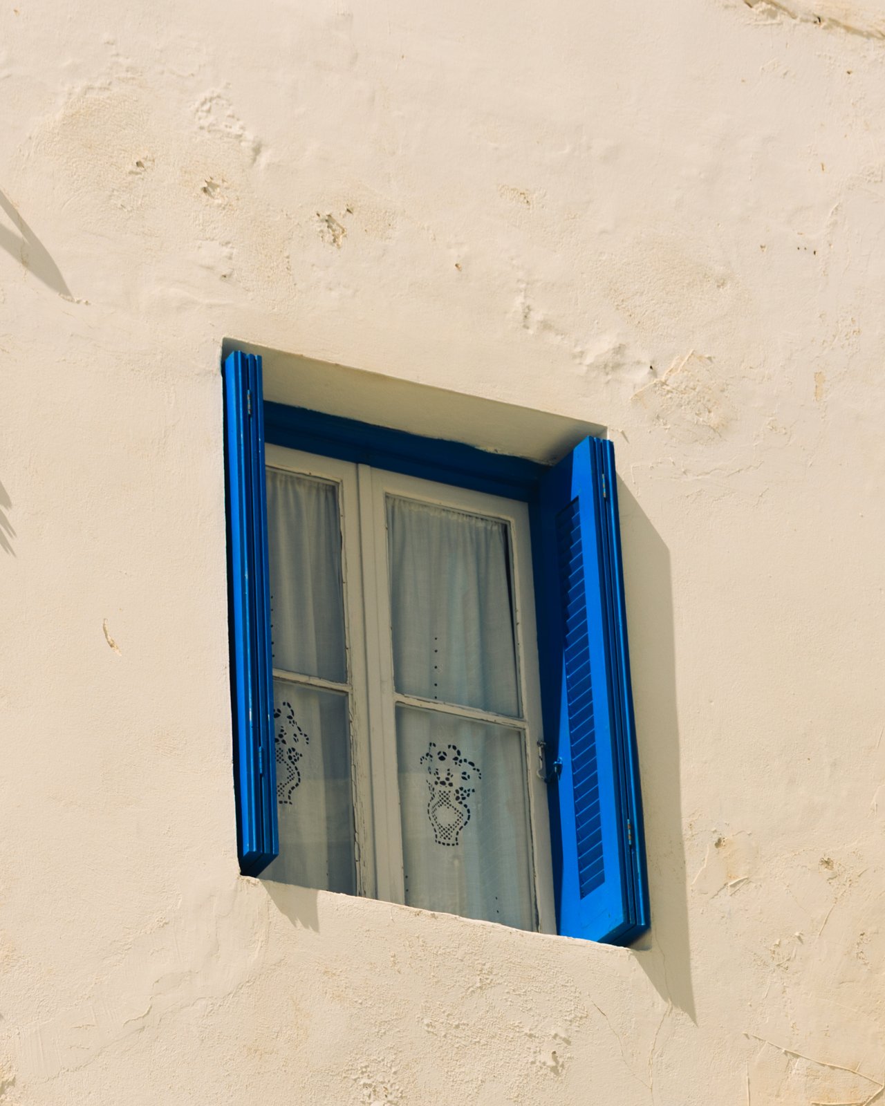 A blue-shuttered window set in a whitewashed wall, Greece