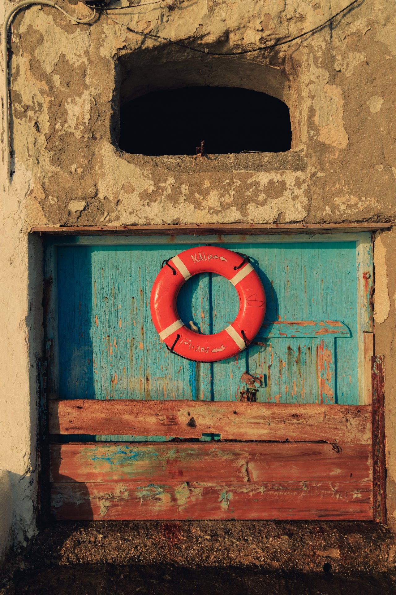 A red life-ring hanging on a weathered turquoise-and-red door, Greece