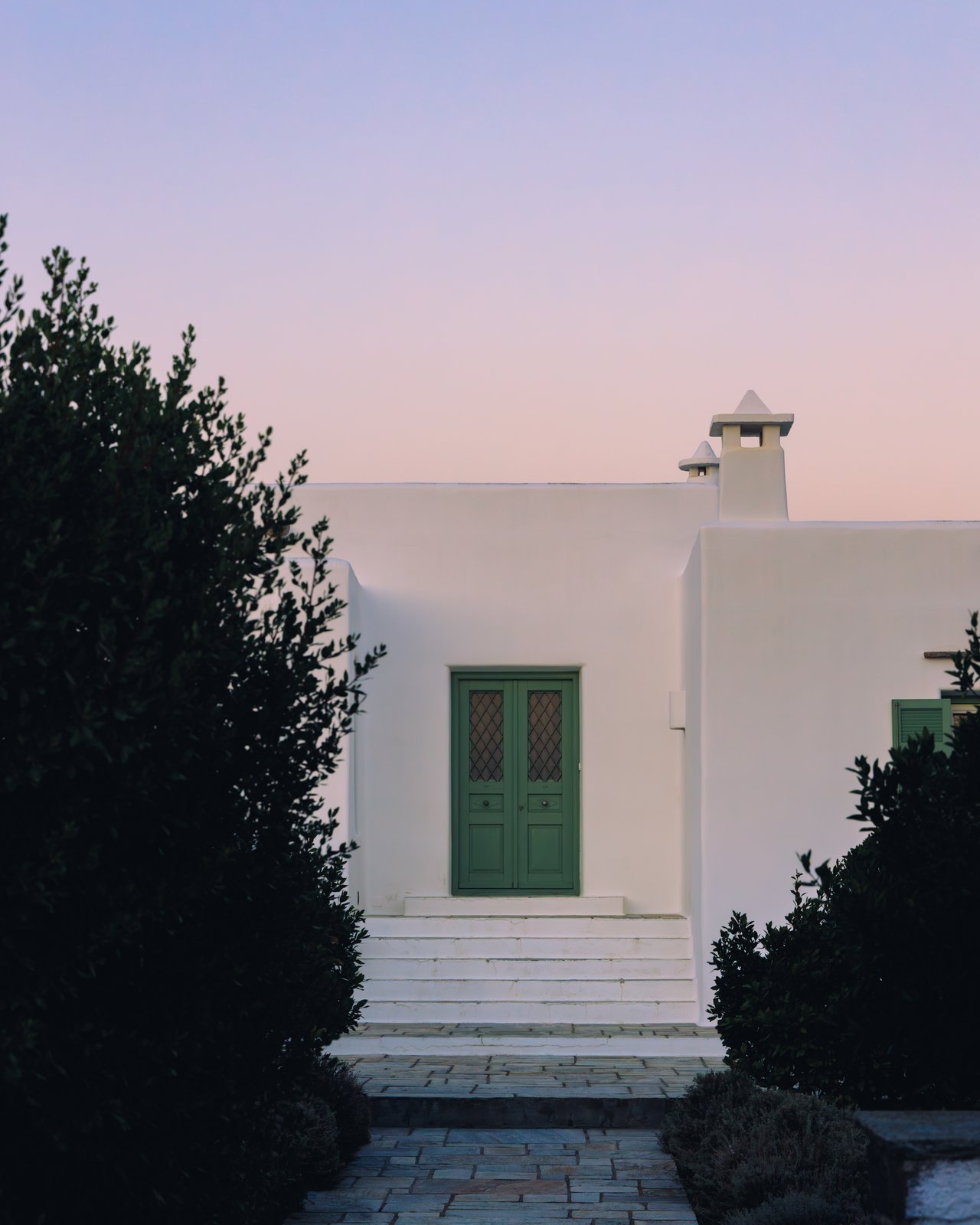 A white Cycladic house with a green door and steps at dusk, Greece
