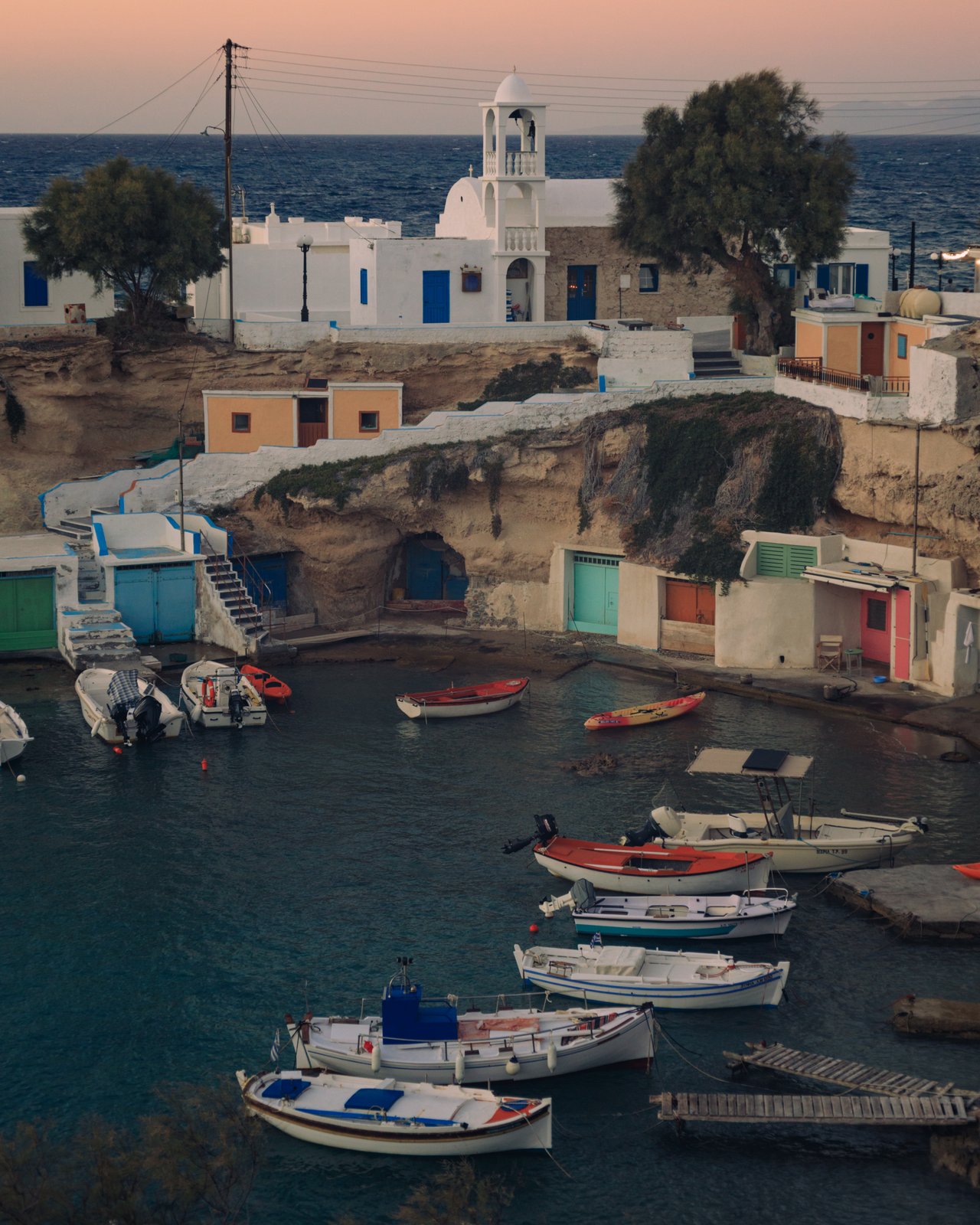 A fishing village of colourful boat garages and moored boats in a cove, Milos, Greece