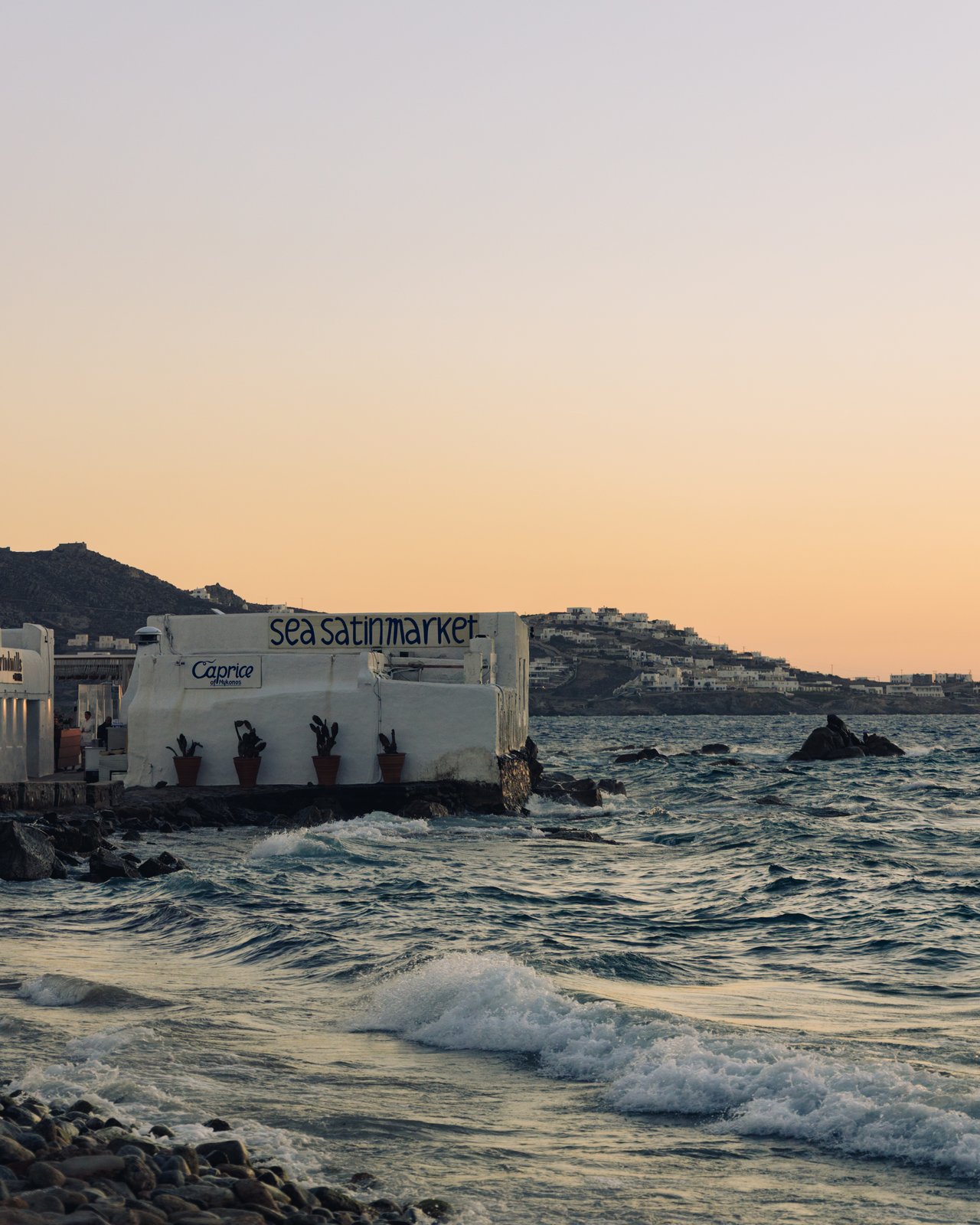 A seaside town of white houses above the waves at golden hour, Mykonos, Greece