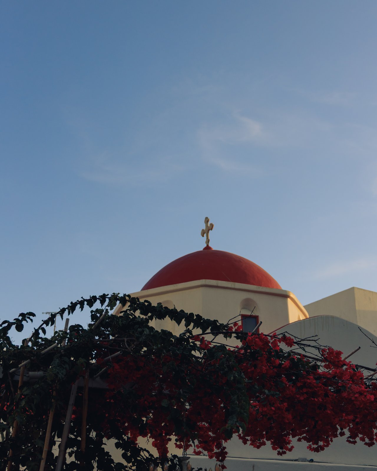 A red-domed white church draped in red bougainvillea, Greece