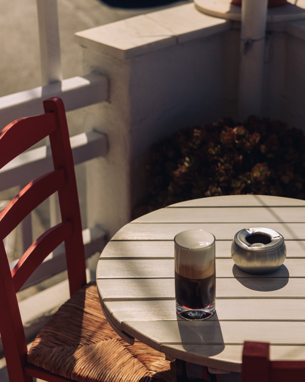 A glass of iced freddo coffee and an ashtray on a sunlit cafe table, Greece