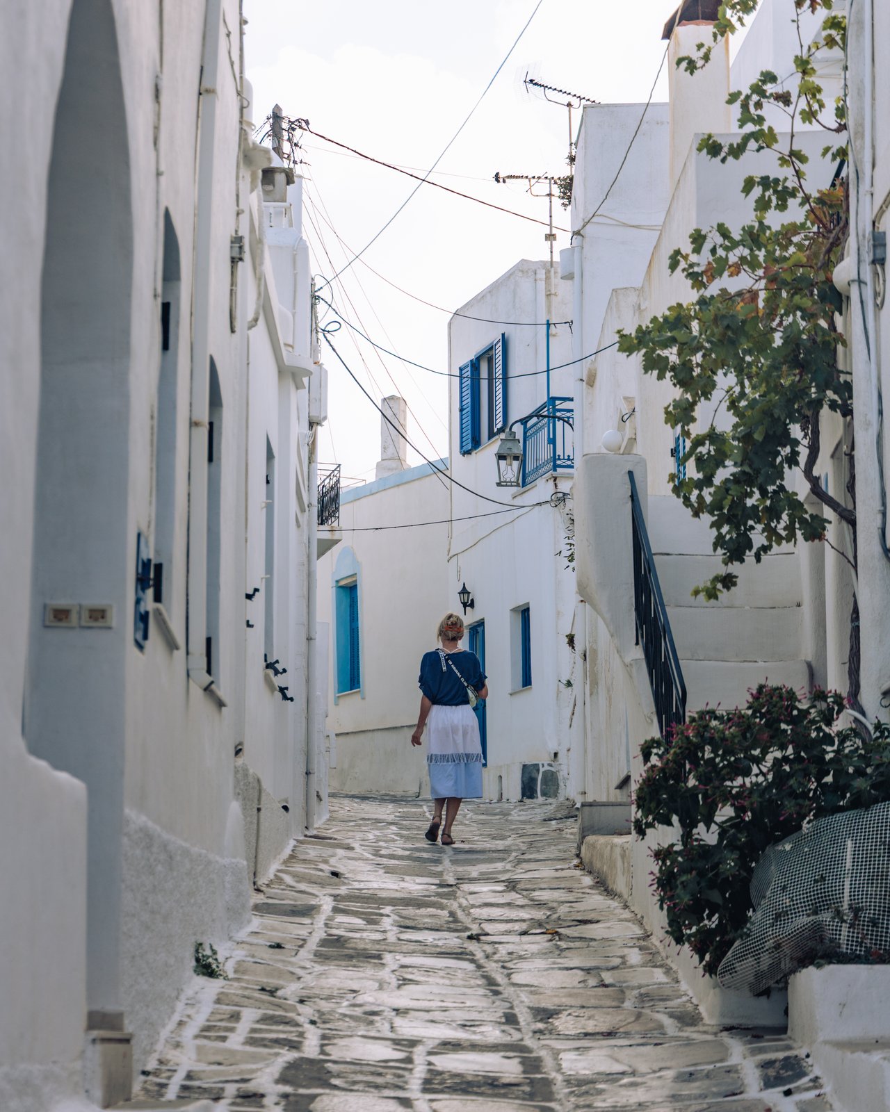 A woman walking a whitewashed marble alley trailing bougainvillea, Greece