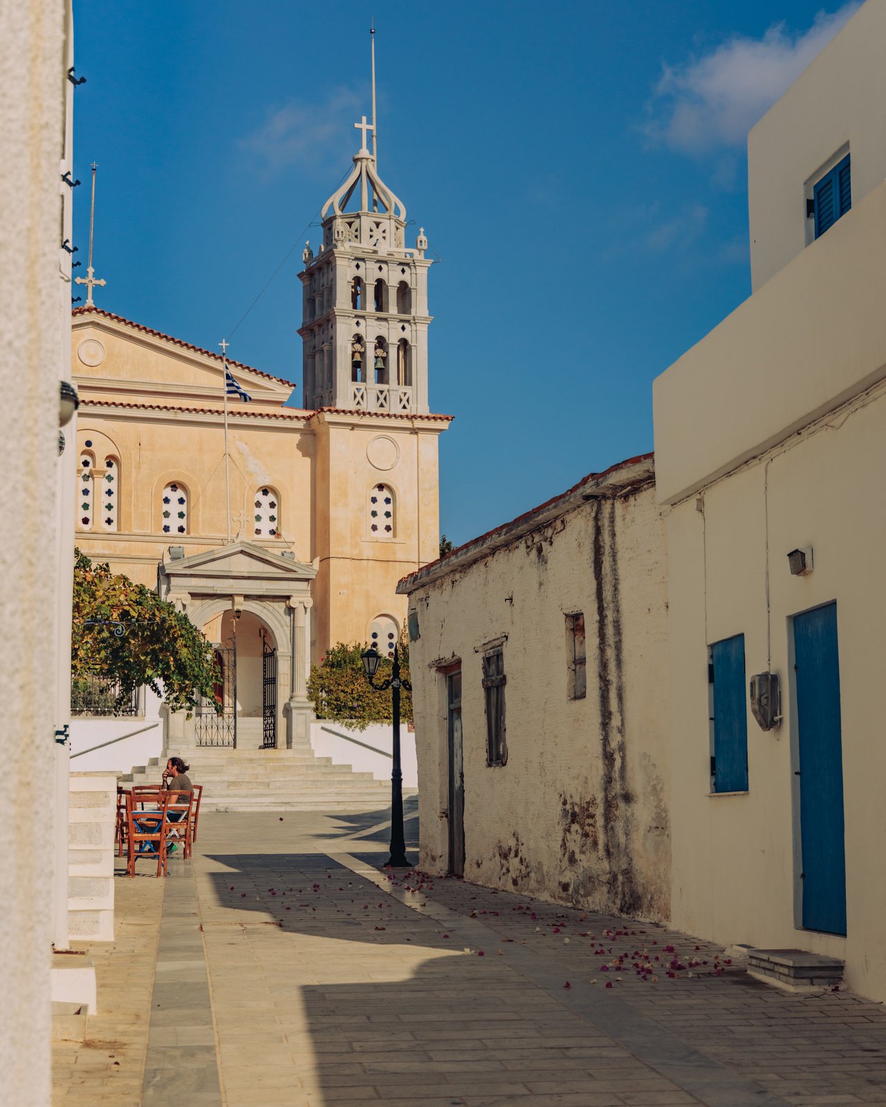 A sandstone church with a tall bell tower at the end of a village street, Paros, Greece