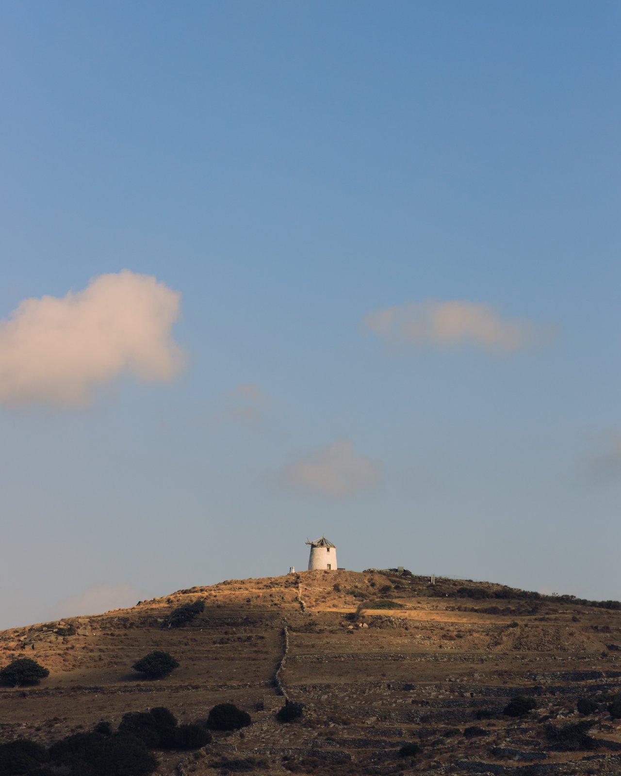 A lone windmill on a bare hilltop at golden hour, Greece