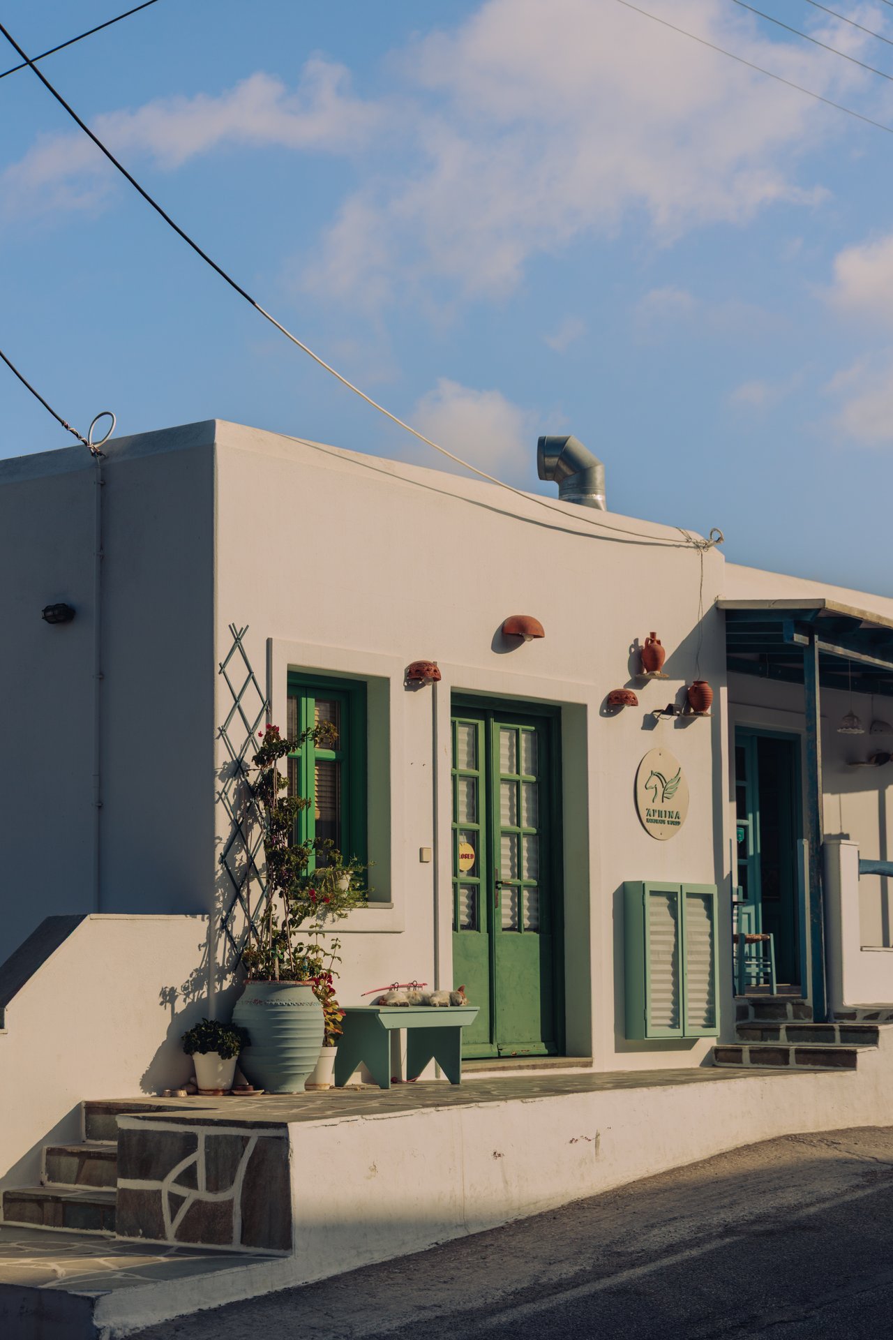 A village lane with a green-doored shop and shuttered houses, Greece