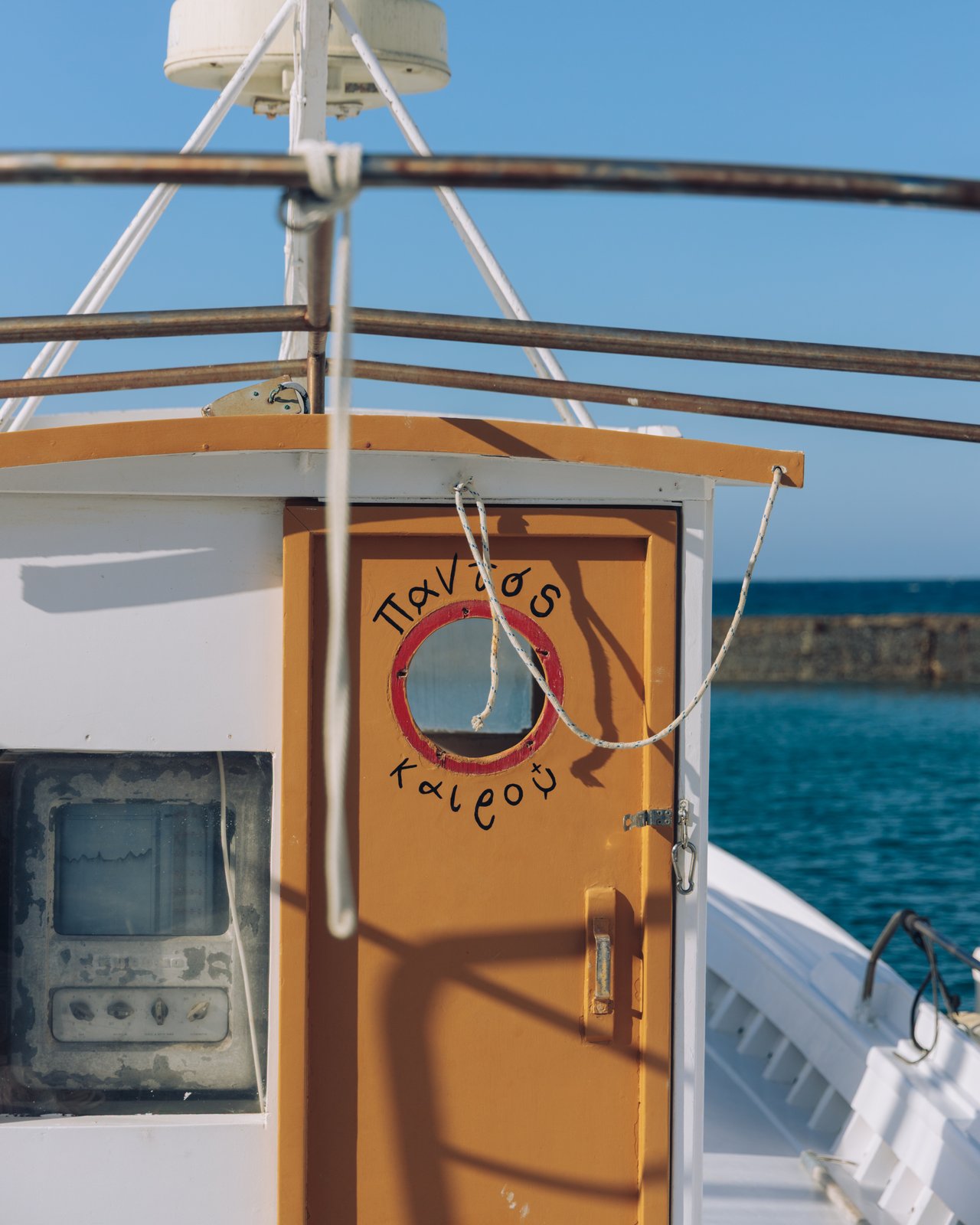 The deck of a ferry with an orange cabin door and a life-ring, the sea beyond, Greece