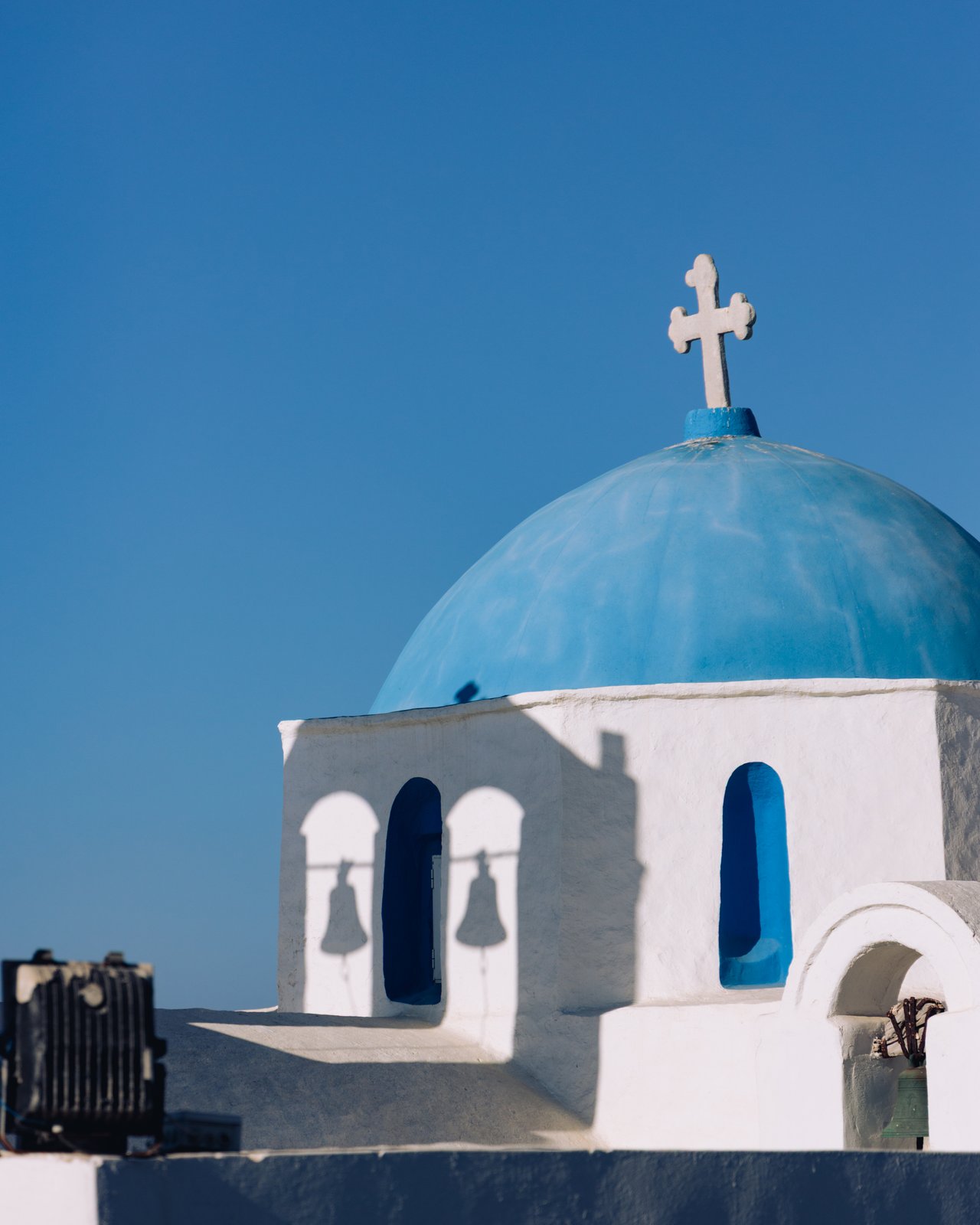 A blue-domed white Cycladic church with a bell-cote against a clear sky, Greece
