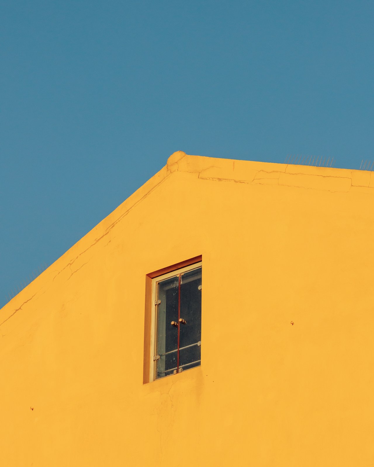 A bright yellow building corner with a single window against blue sky, Greece