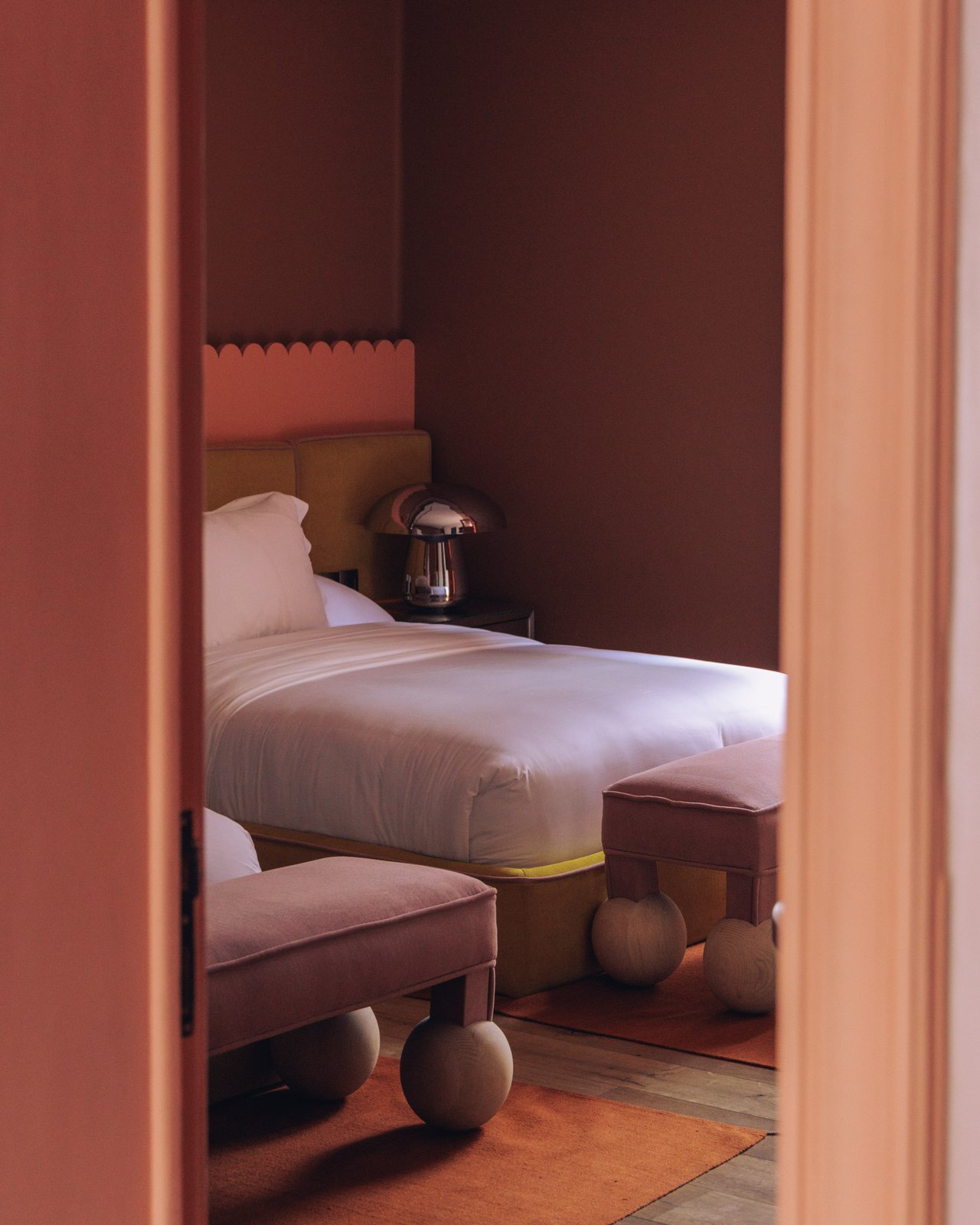 A bed and ball-footed ottoman glimpsed through a doorway in a terracotta room, Ignacia Guest House