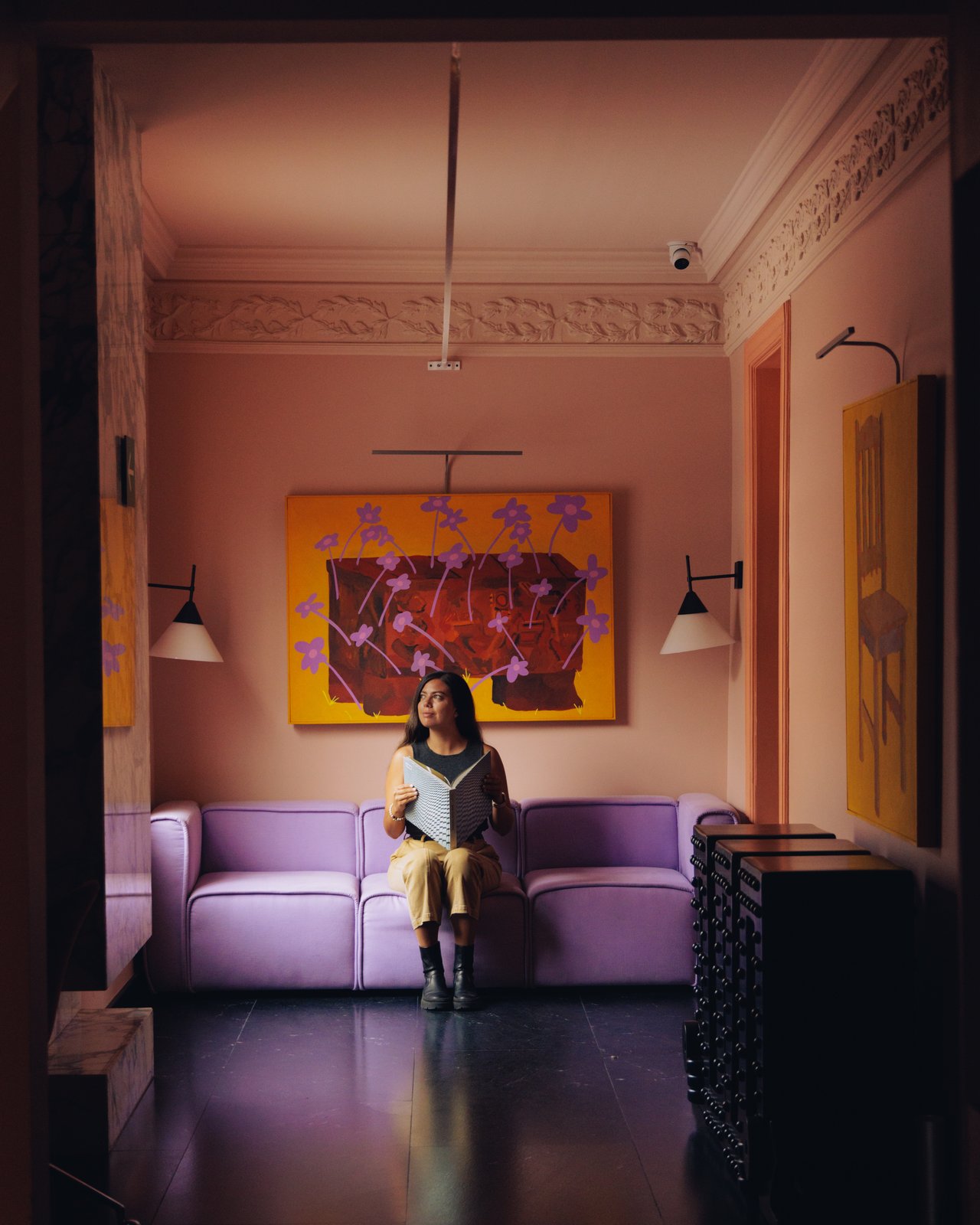 A woman reading on the lilac sofa beneath the lounge artwork, Ignacia Guest House