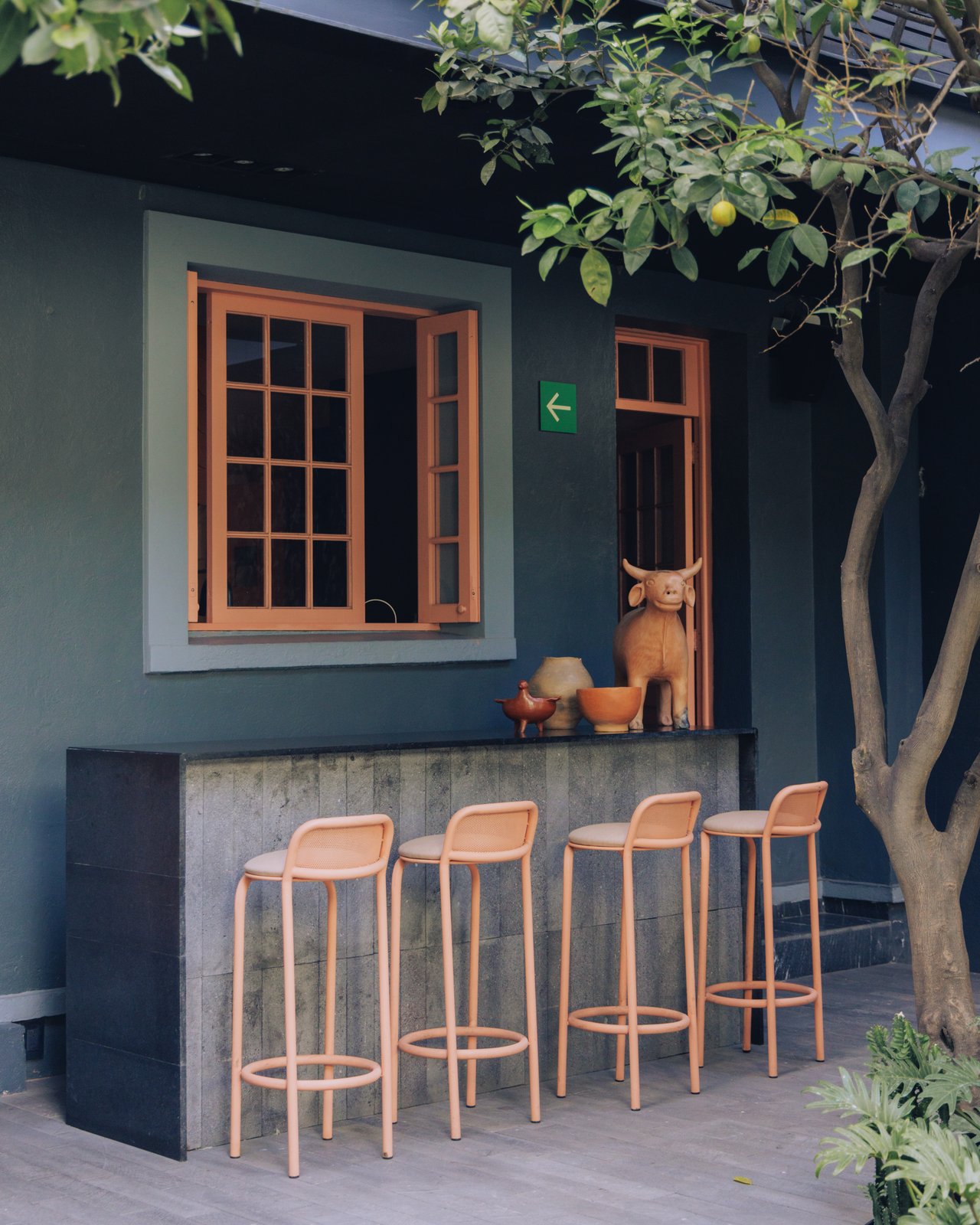 An outdoor bar with pink stools against a teal wall by a lemon tree, Ignacia Guest House