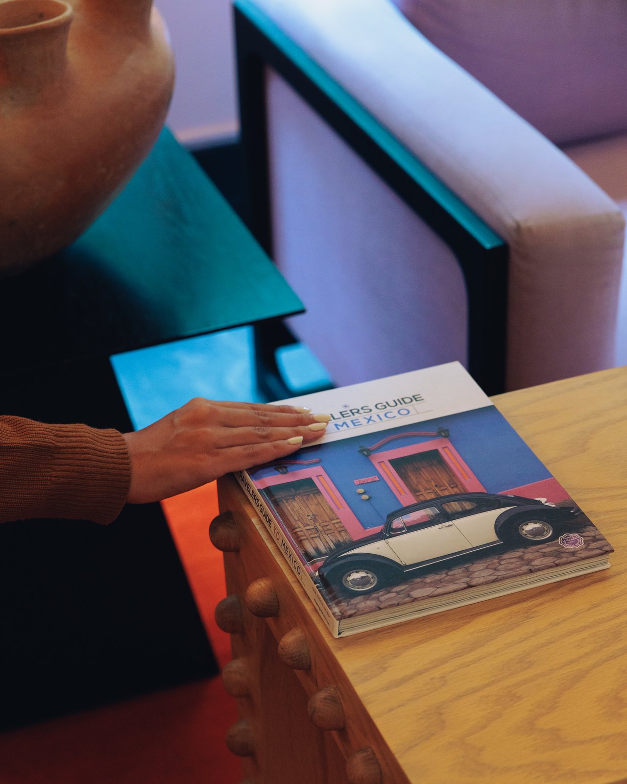 A hand resting on a 'Travelers' Guide to Mexico' book on a wood table, Ignacia Guest House