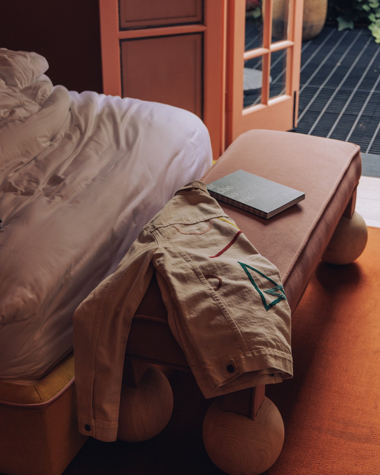 A khaki jacket and book on the ball-footed ottoman at the foot of a bed, Ignacia Guest House