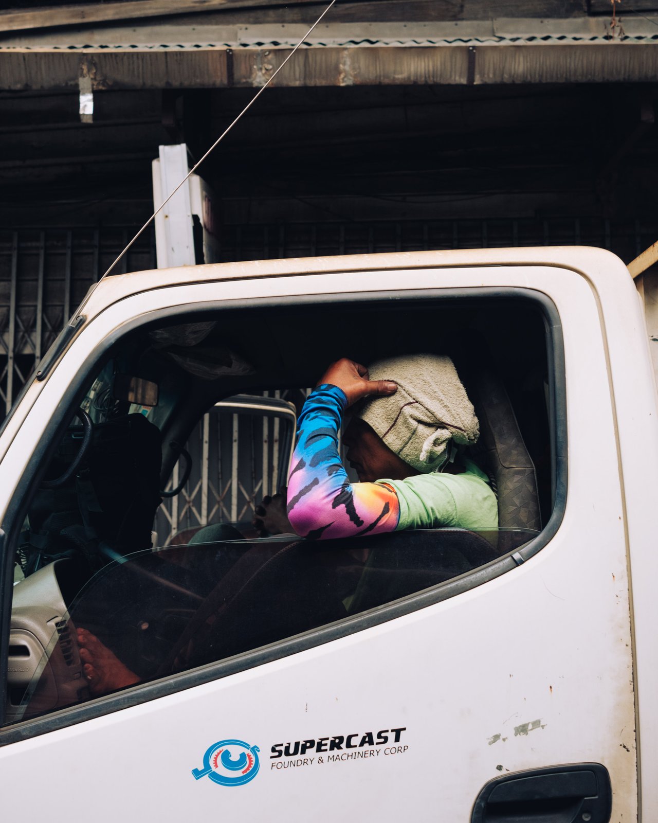 A man napping in the cab of a parked delivery truck, an arm resting on the window, Manila