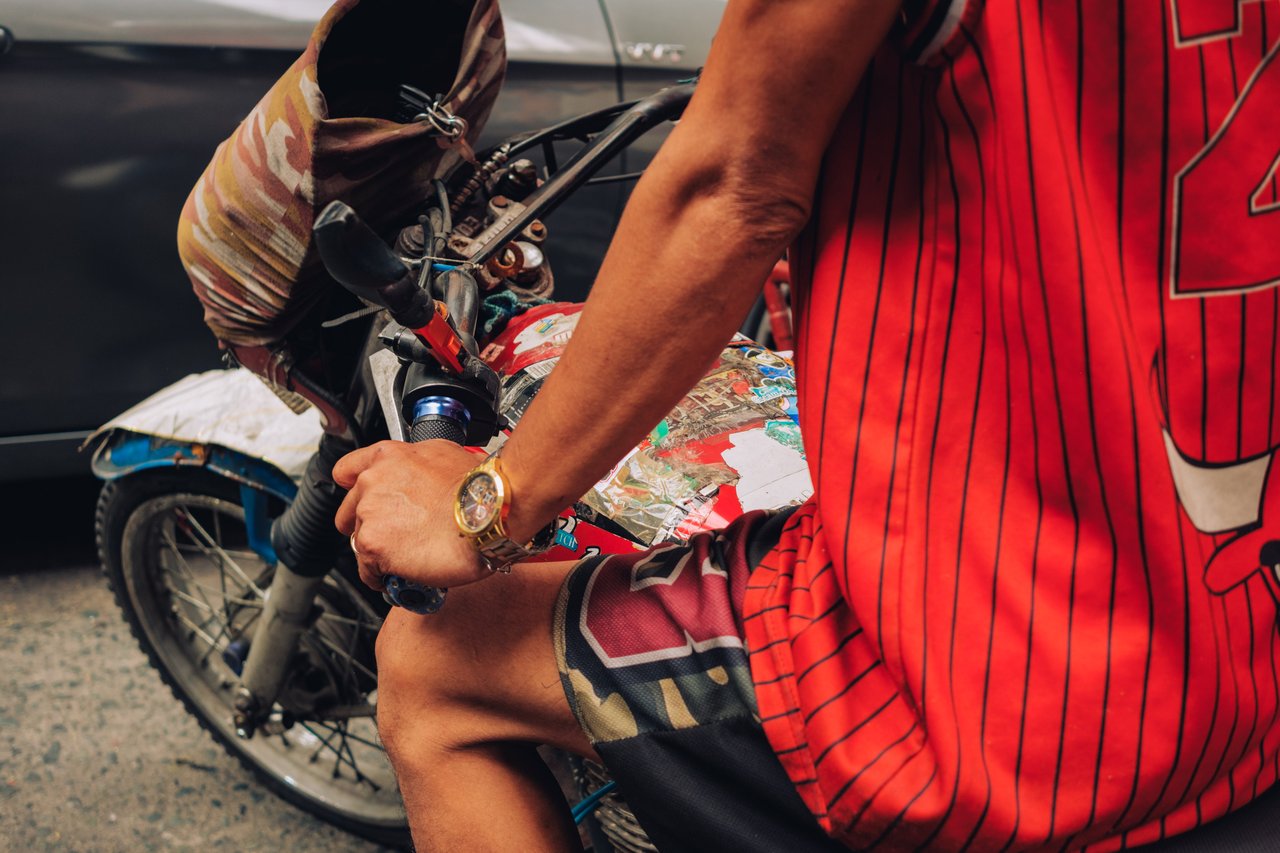 A man in a red striped jersey astride a motorbike, holding a bundle, Manila