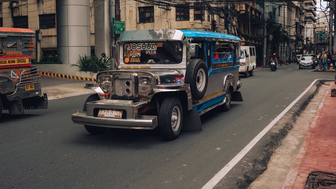 A chrome-and-blue jeepney riding down a quiet Manila street in the morning