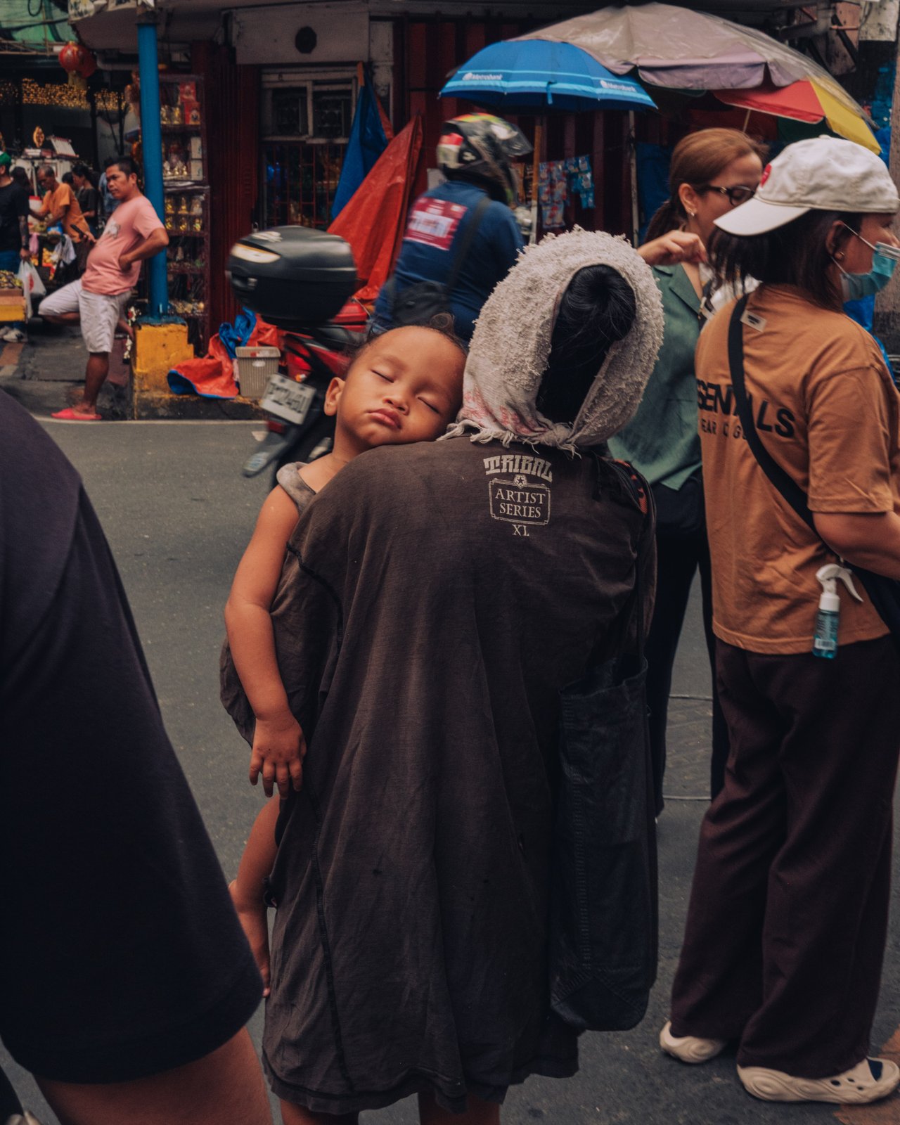 A toddler asleep in a sling on a caregiver's back at a Manila market