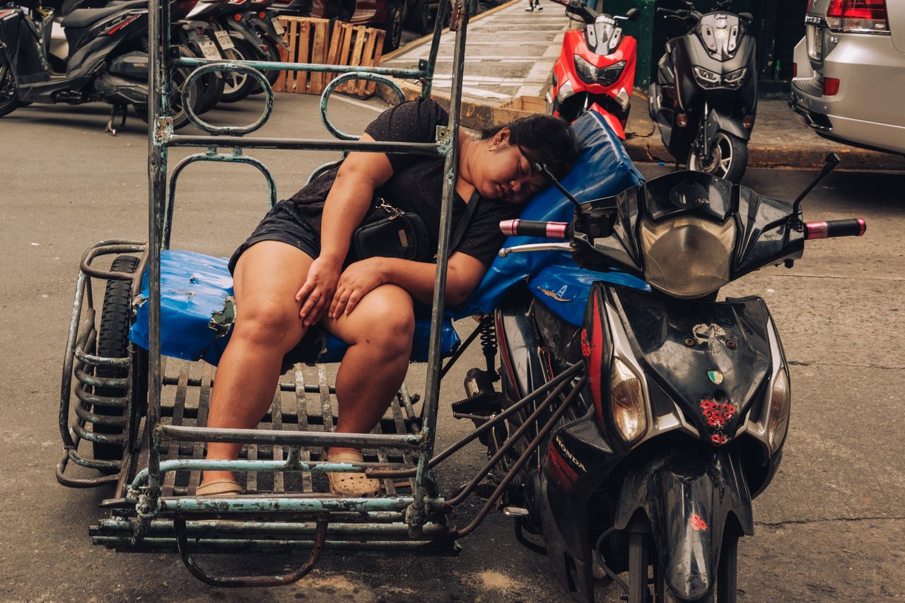 A man asleep on the sidecar of his parked pedicab in the street, Manila