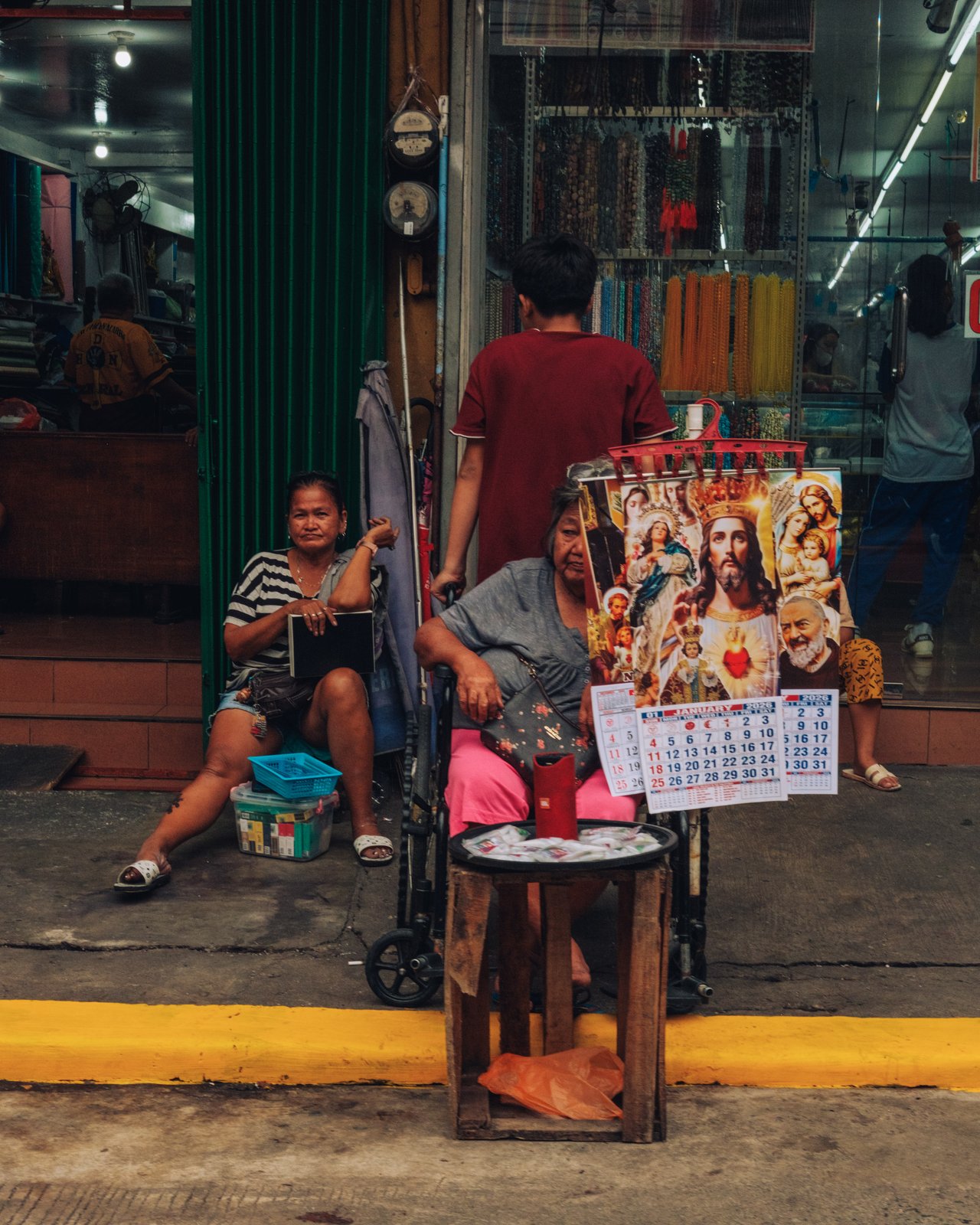Two women at a sidewalk stall of religious calendars, one seated in a wheelchair, Manila