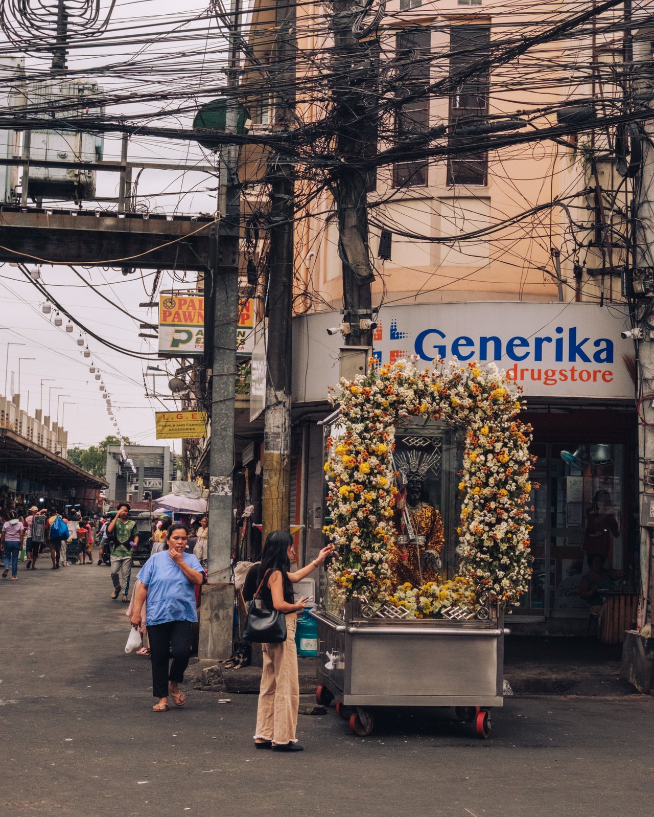 A flower-wreath cart beside a Generika drugstore, an LRT viaduct behind, Manila