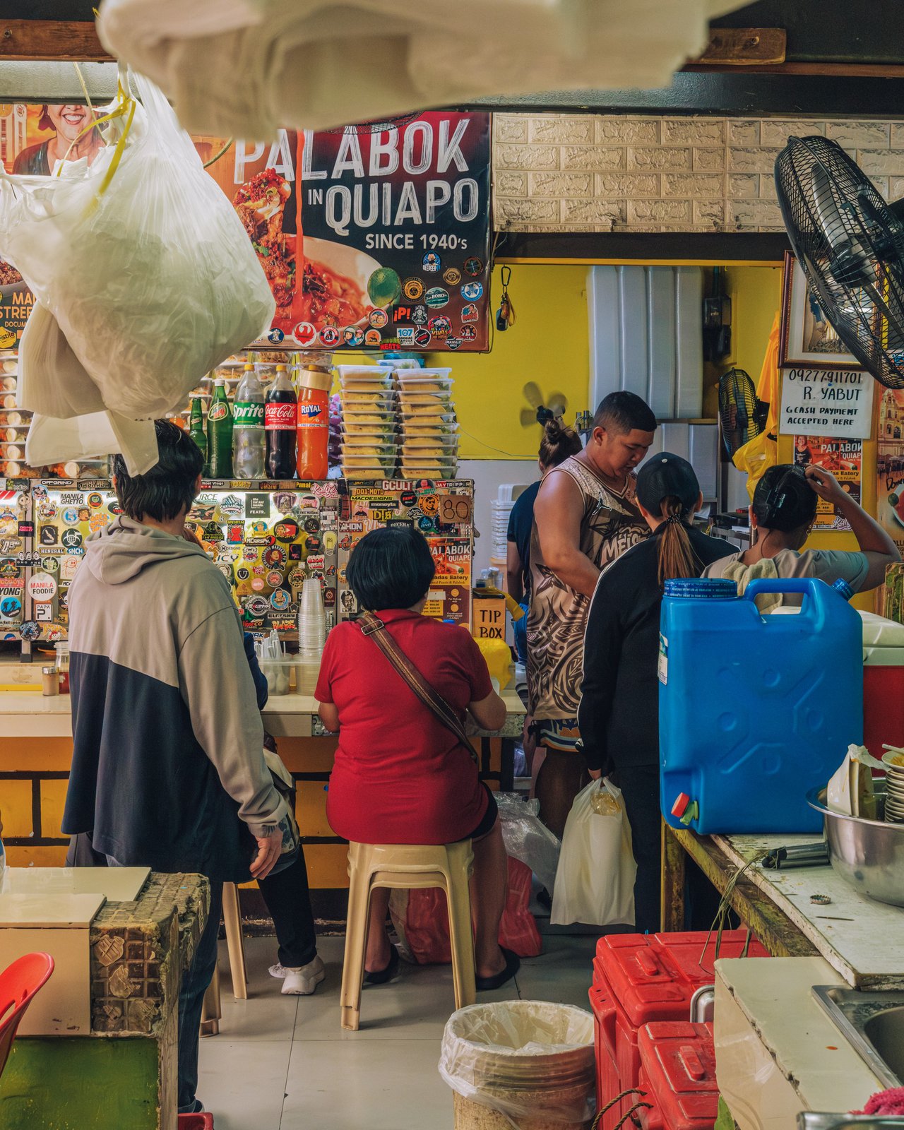 Customers at a palabok stall in Quiapo, takeaway bags hanging overhead, Manila
