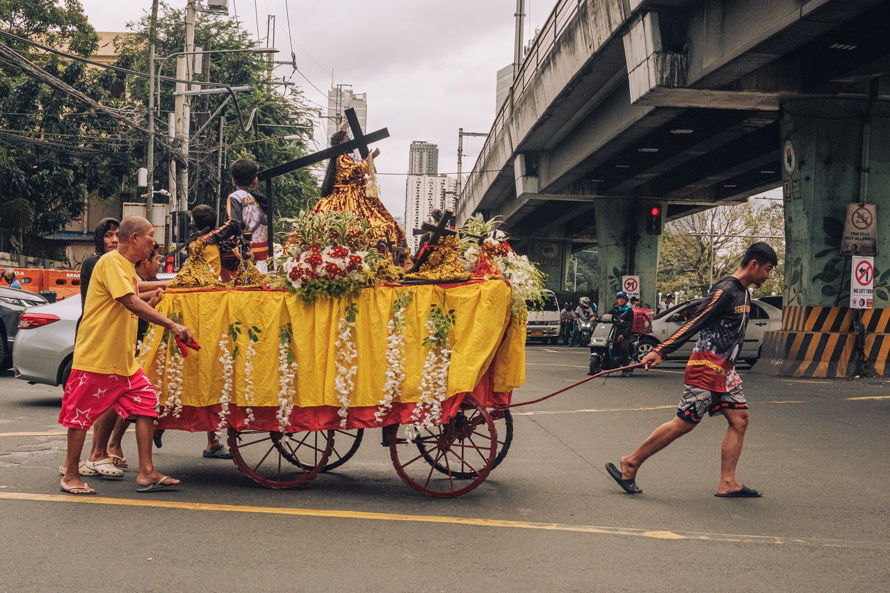 Men pulling a flower-draped religious procession cart under the LRT tracks, Manila