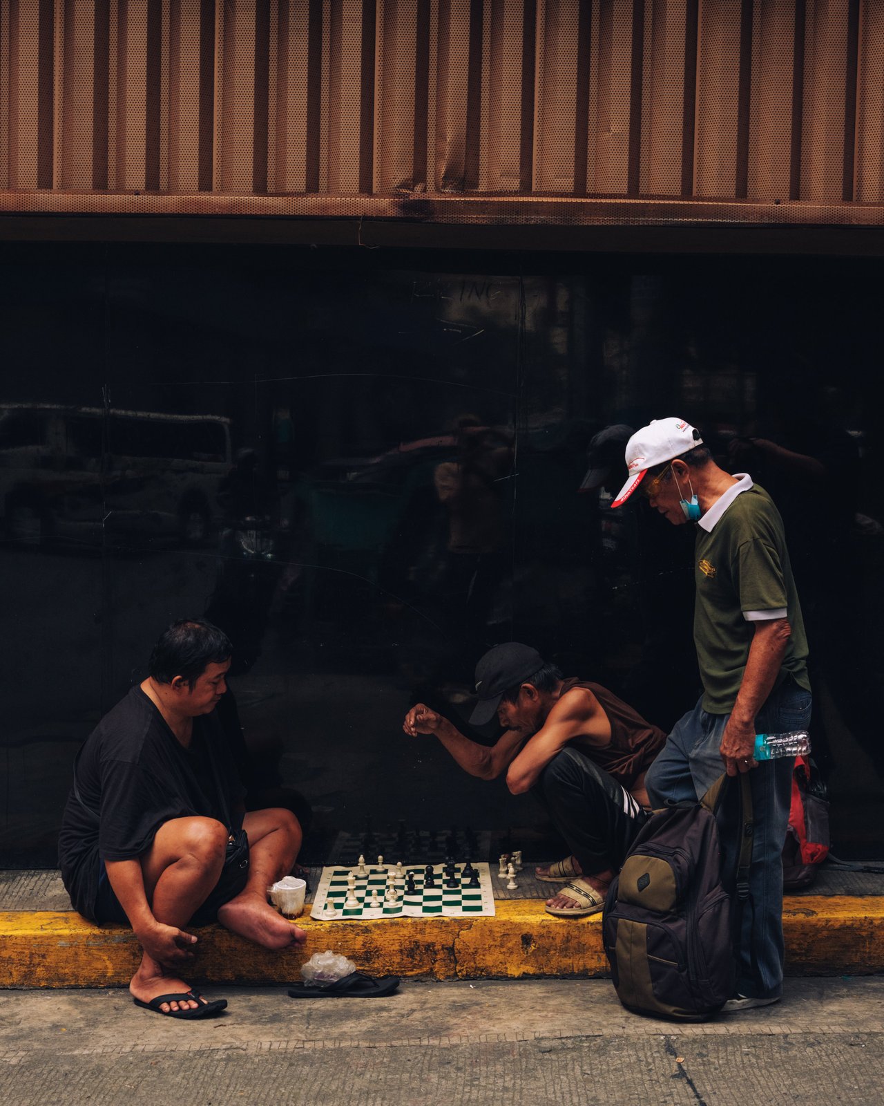 Two men playing chess on a curb while another looks on, Manila