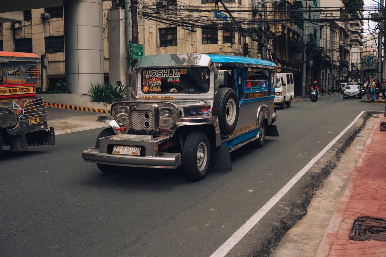 A jeepney coming down a jeepney-lined street beneath a tangle of overhead wires, Manila