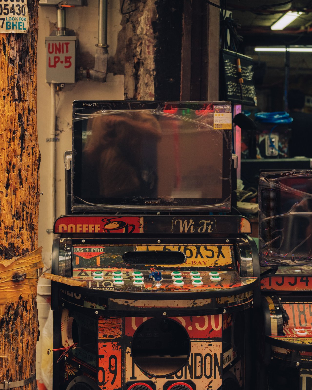 A battered coin-op karaoke jukebox plastered with licence plates on a grimy wall, Manila