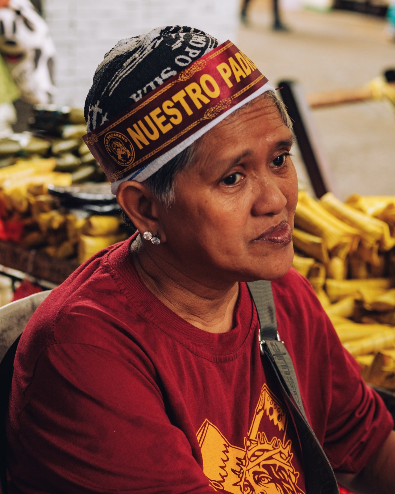 A woman in a red Black Nazarene devotee's headband at a market, dried goods behind, Manila