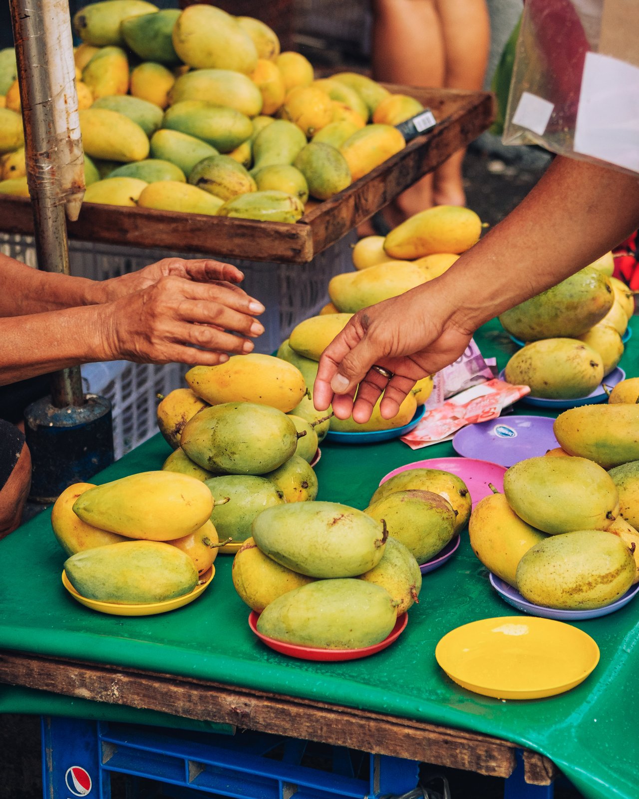 A vendor arranging green-and-yellow mangoes heaped on a cart, Manila