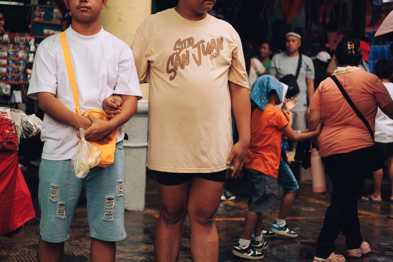 A boy and a man in a crowded market street, shoppers pressing past, Manila