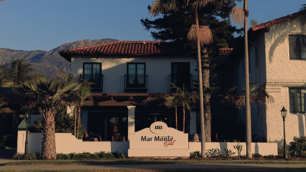 The Mar Monte Hotel's white Spanish-Colonial facade and red-tile roof at golden hour, palms and the Santa Barbara mountains behind