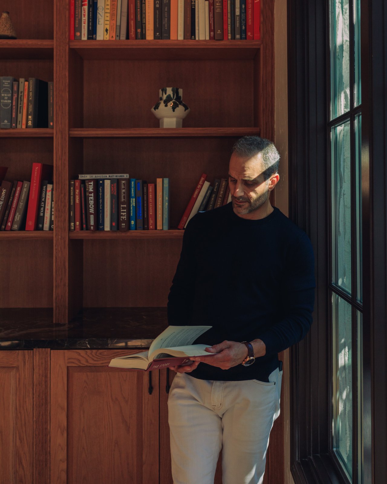 A man reading by tall windows in front of the wood library shelves at the Mar Monte Hotel, Santa Barbara