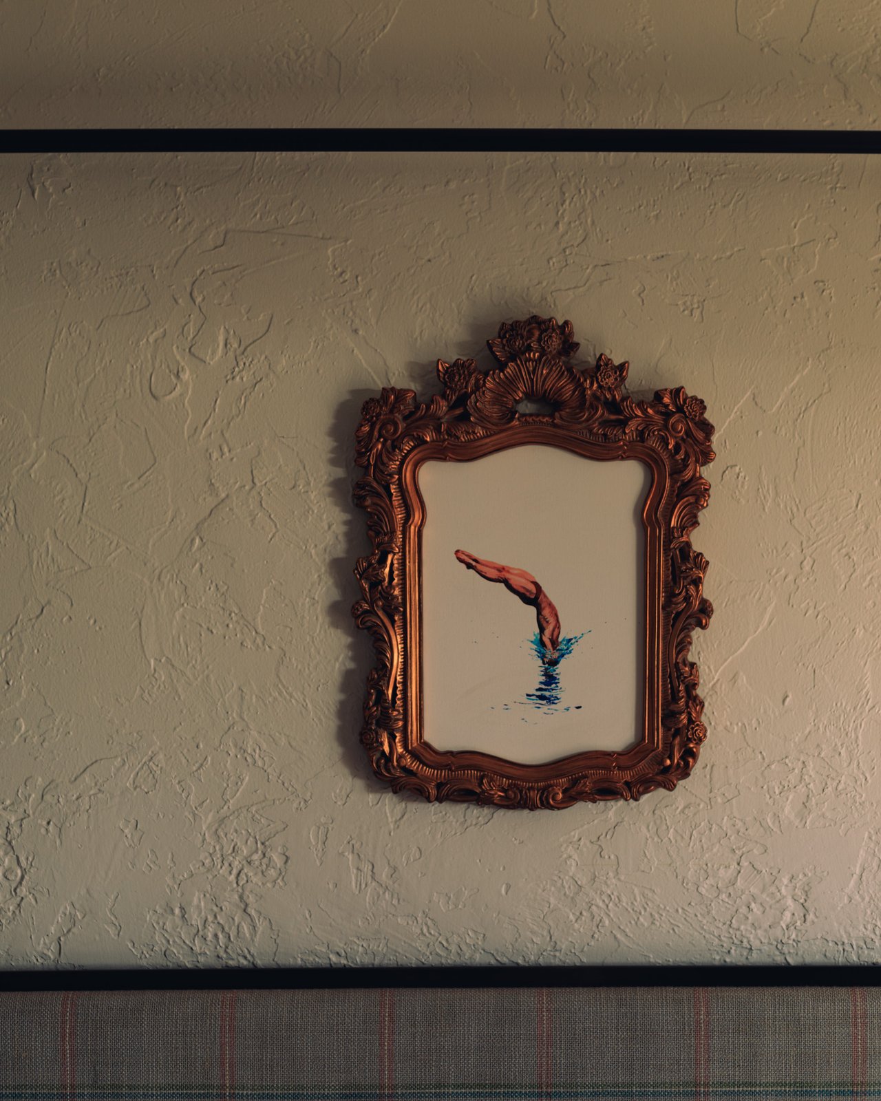 A framed vintage print of a diver hung on a textured stucco wall