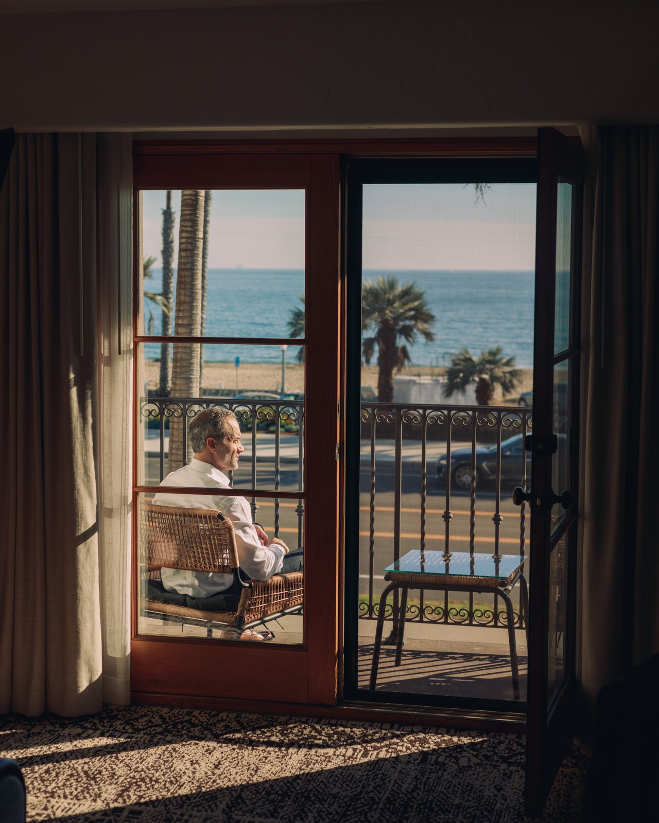A guest on a balcony with French doors open to Cabrillo Boulevard, palms and the ocean at Santa Barbara