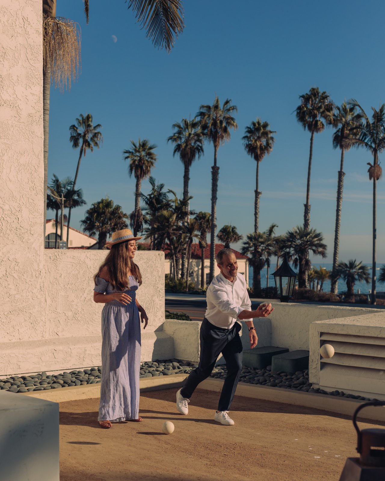 A couple playing bocce on a palm-lined court under a clear blue sky at the Mar Monte Hotel