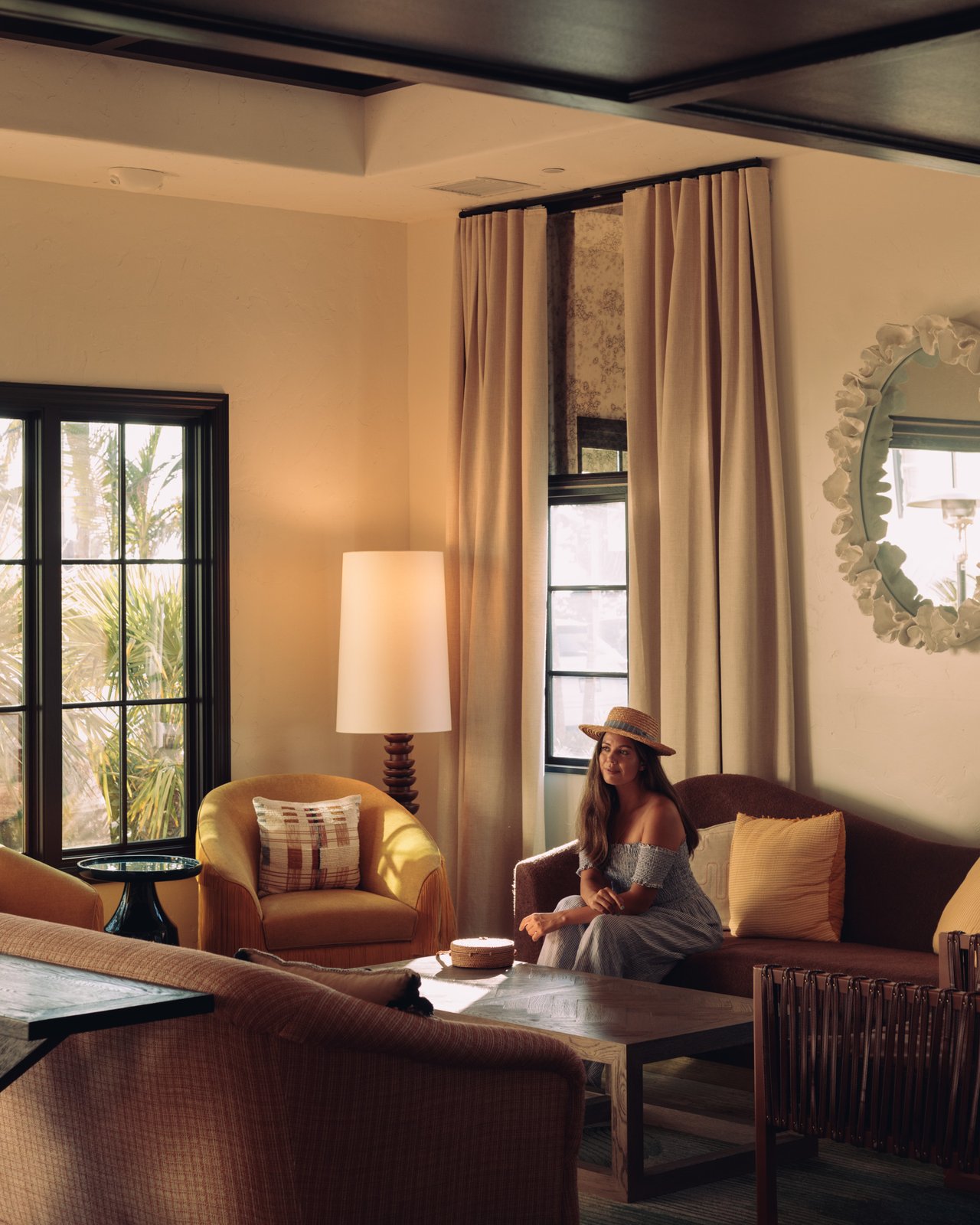 A woman on a sofa in a warm guest-suite living room, table lamp lit and armchair alongside