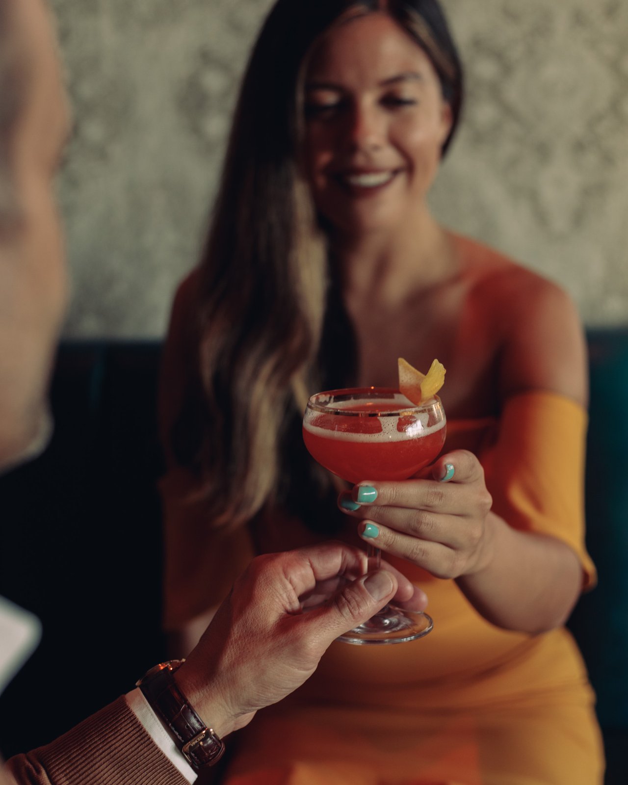 A close toast — a woman in an orange dress holding a red cocktail