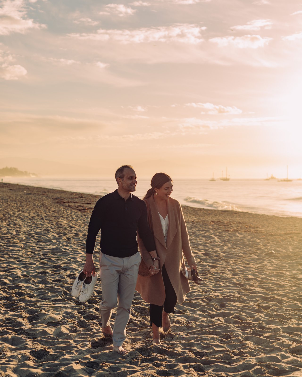 A couple walking hand in hand along East Beach at sunset, shoes in hand, Santa Barbara
