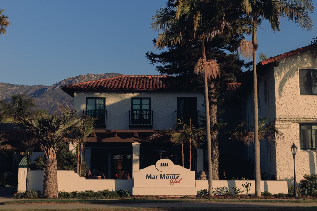 The Mar Monte Hotel's Spanish-Colonial exterior and sign framed by tall palms and mountains