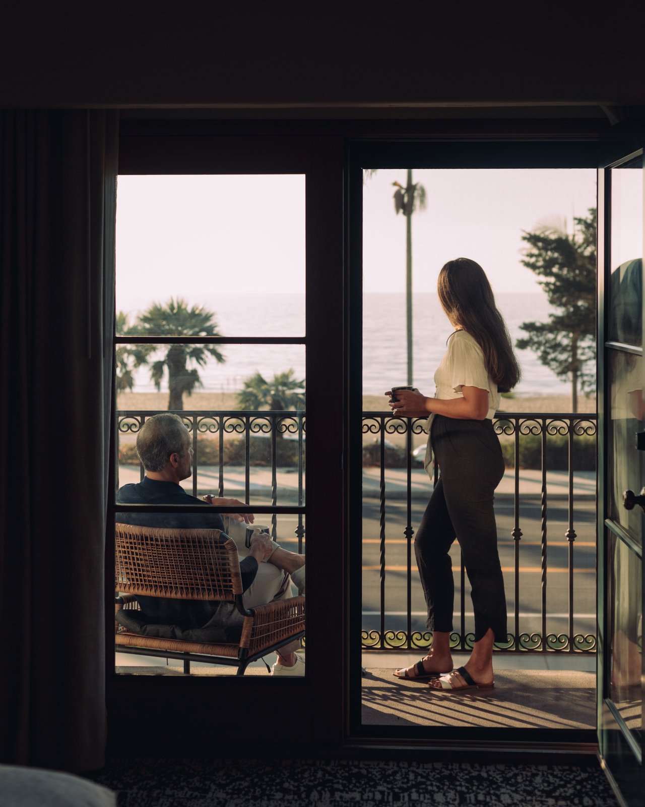 A woman on a guest balcony overlooking Cabrillo Boulevard and the ocean, a man seated reading