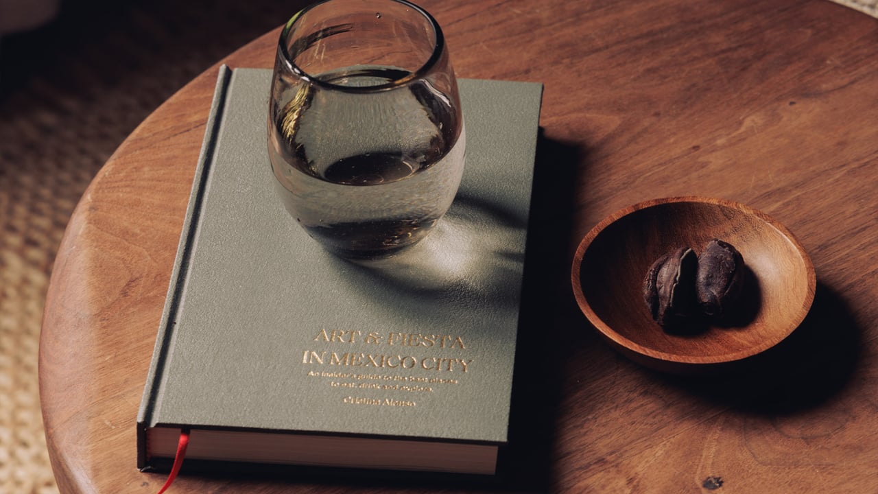 A glass of water, a chocolate in a wood bowl and a green architecture book on a round table at Octavia Casa, Mexico City