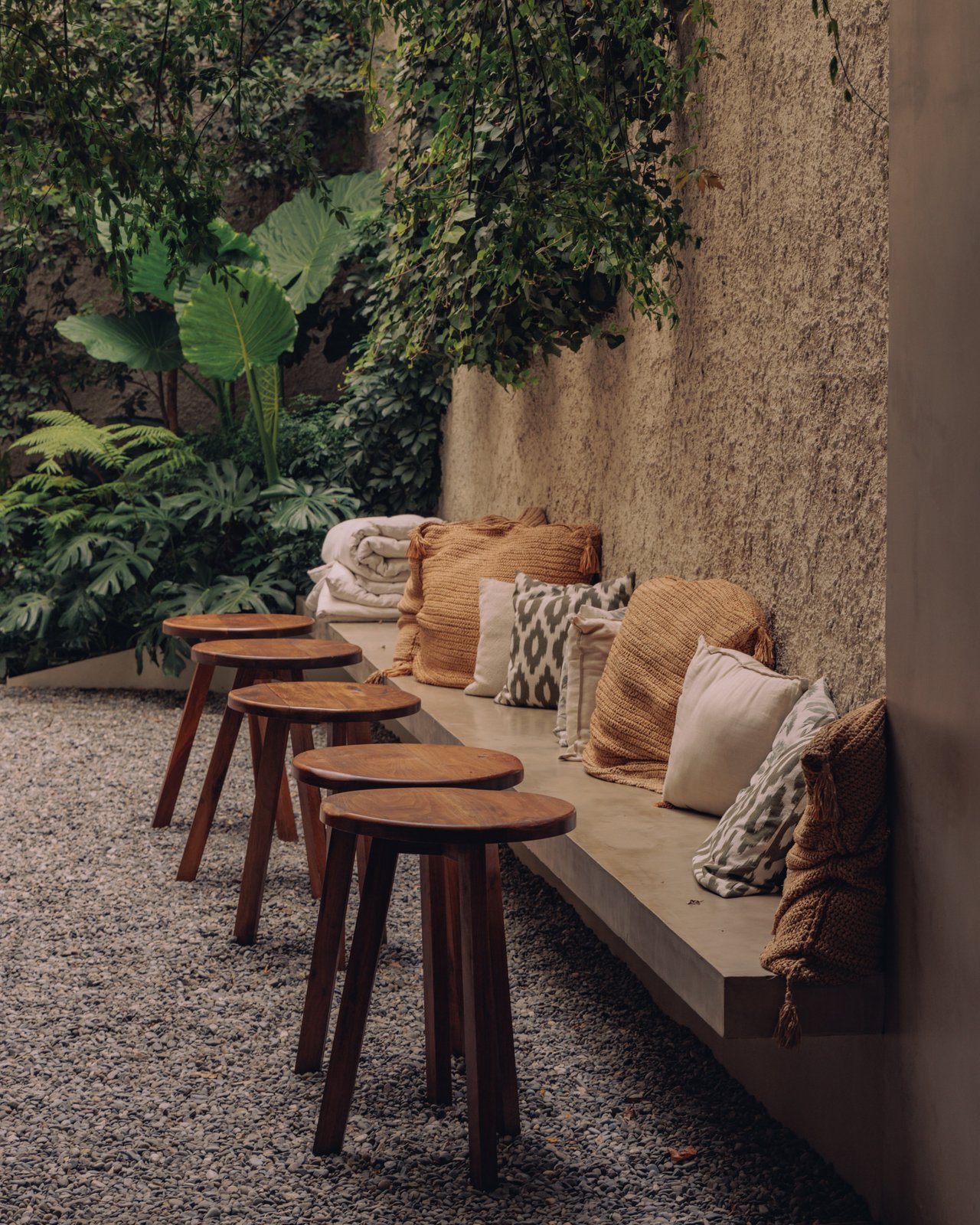 A leafy branch in a sculptural stone vase on a round side table against a bare plaster wall